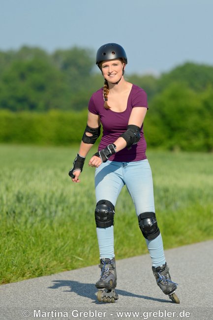 Junge Frau mit Helm und Schoner beim Inline Skating auf einer kleinen Straße 