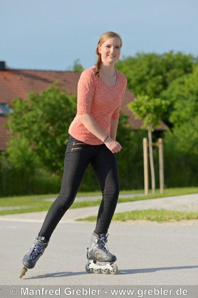 Junge Frau beim Inline Skating auf einer kleinen Straße 